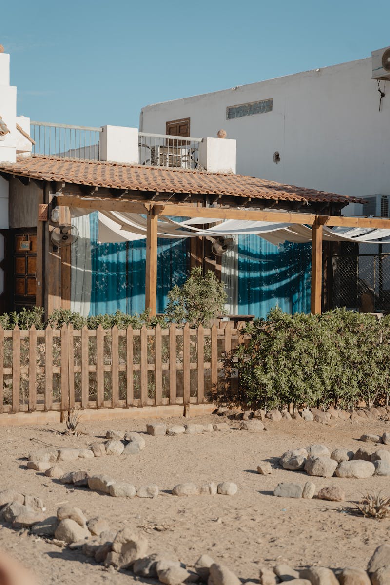 Charming Mediterranean house with wooden fence and plants under clear blue sky.